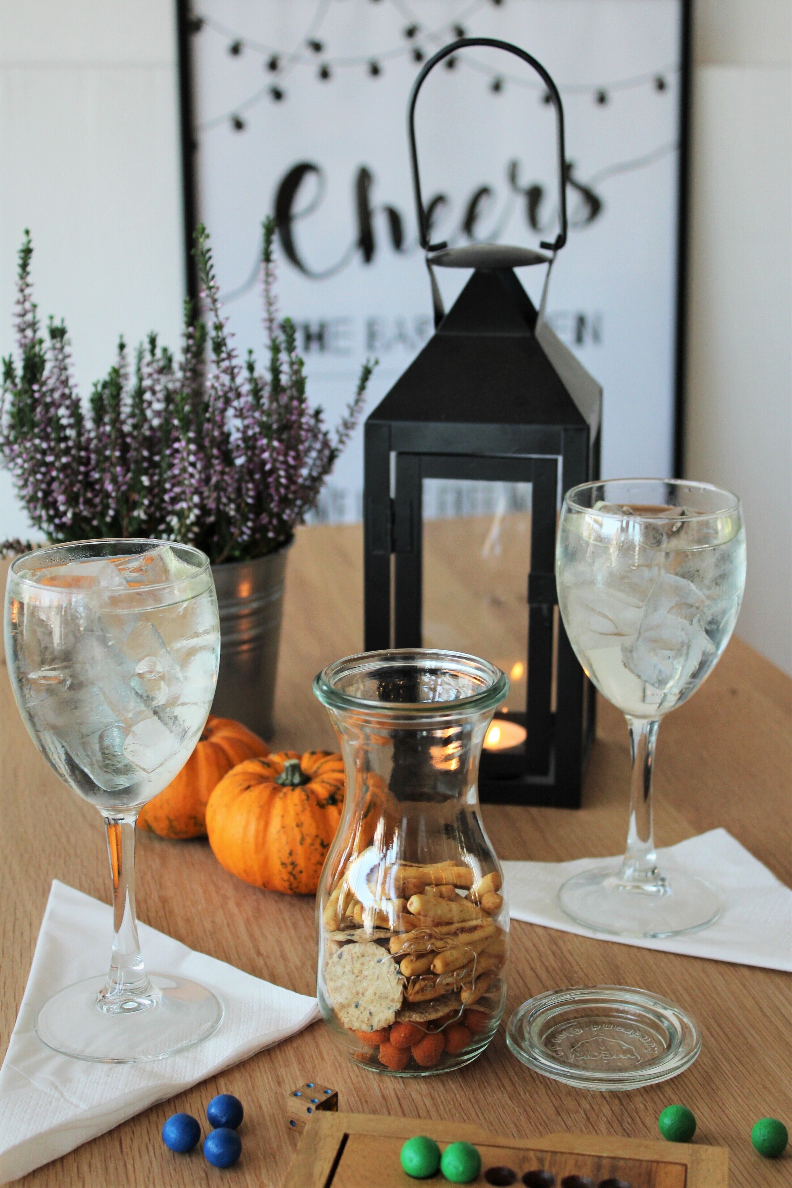 A table with two glasses of water, a jar of cookies, a pumpkin, and a lantern.