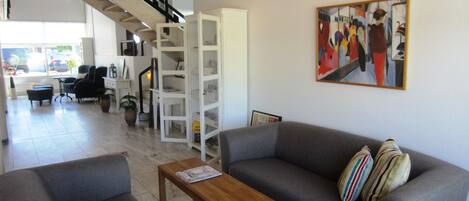 Amplia sala de estar con un sofá gris, una mesa de centro de madera y una escalera que sube a un nivel superior.