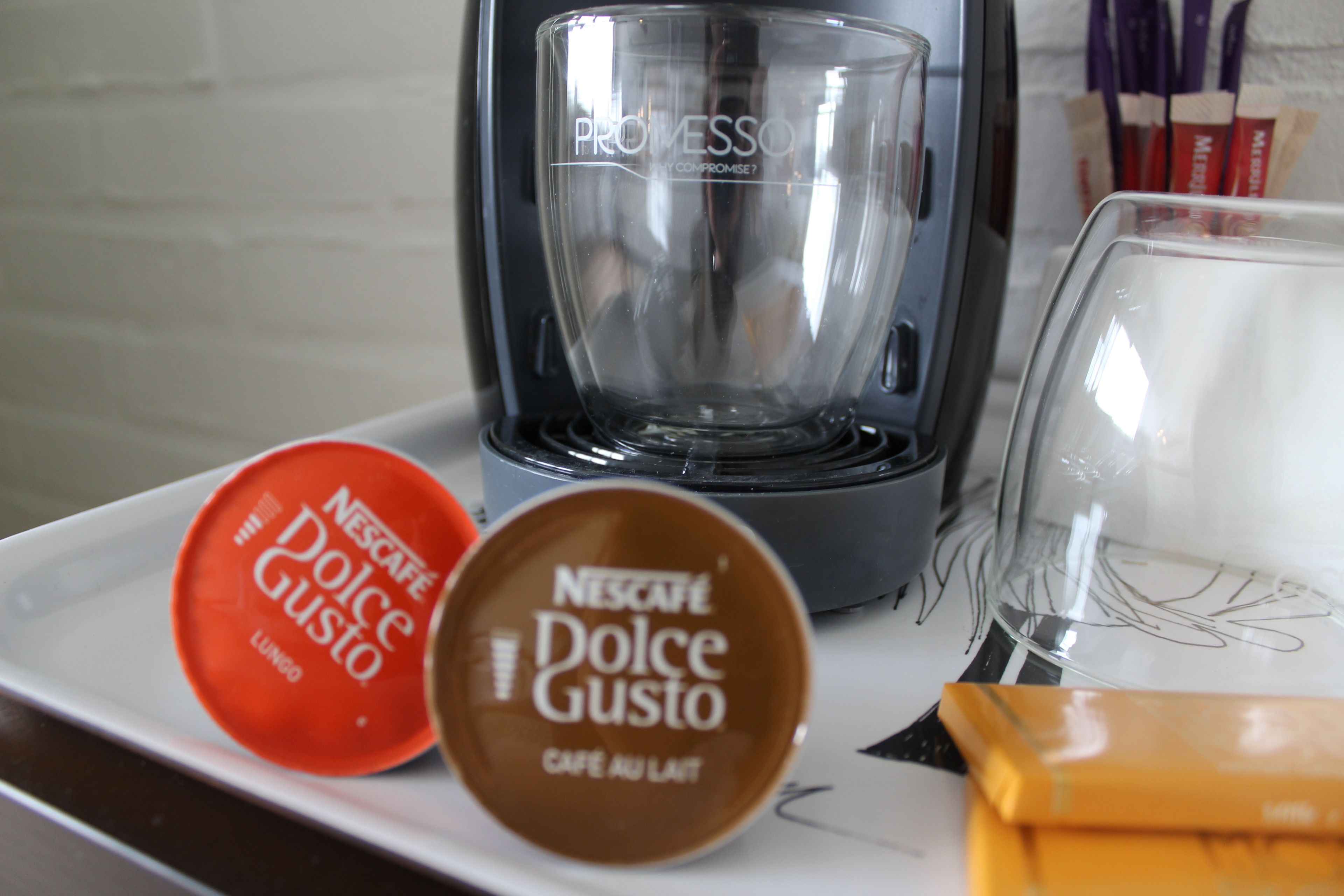 Una cafetera, dos cápsulas Nescafé Dolce Gusto y un vaso sobre una bandeja.
