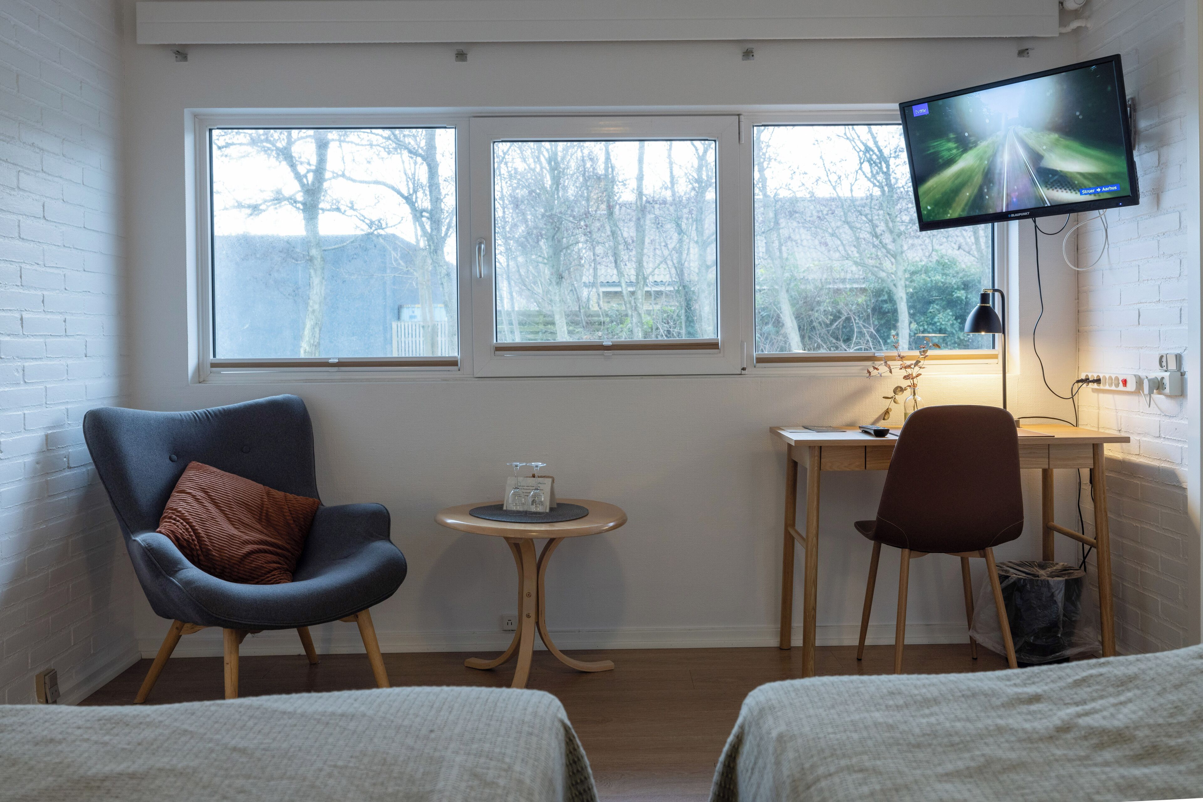 Una habitación con dos camas, un escritorio, una silla, un televisor y tres ventanas.