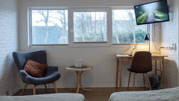 Una habitación con dos camas, un escritorio, una silla, un televisor y tres ventanas.