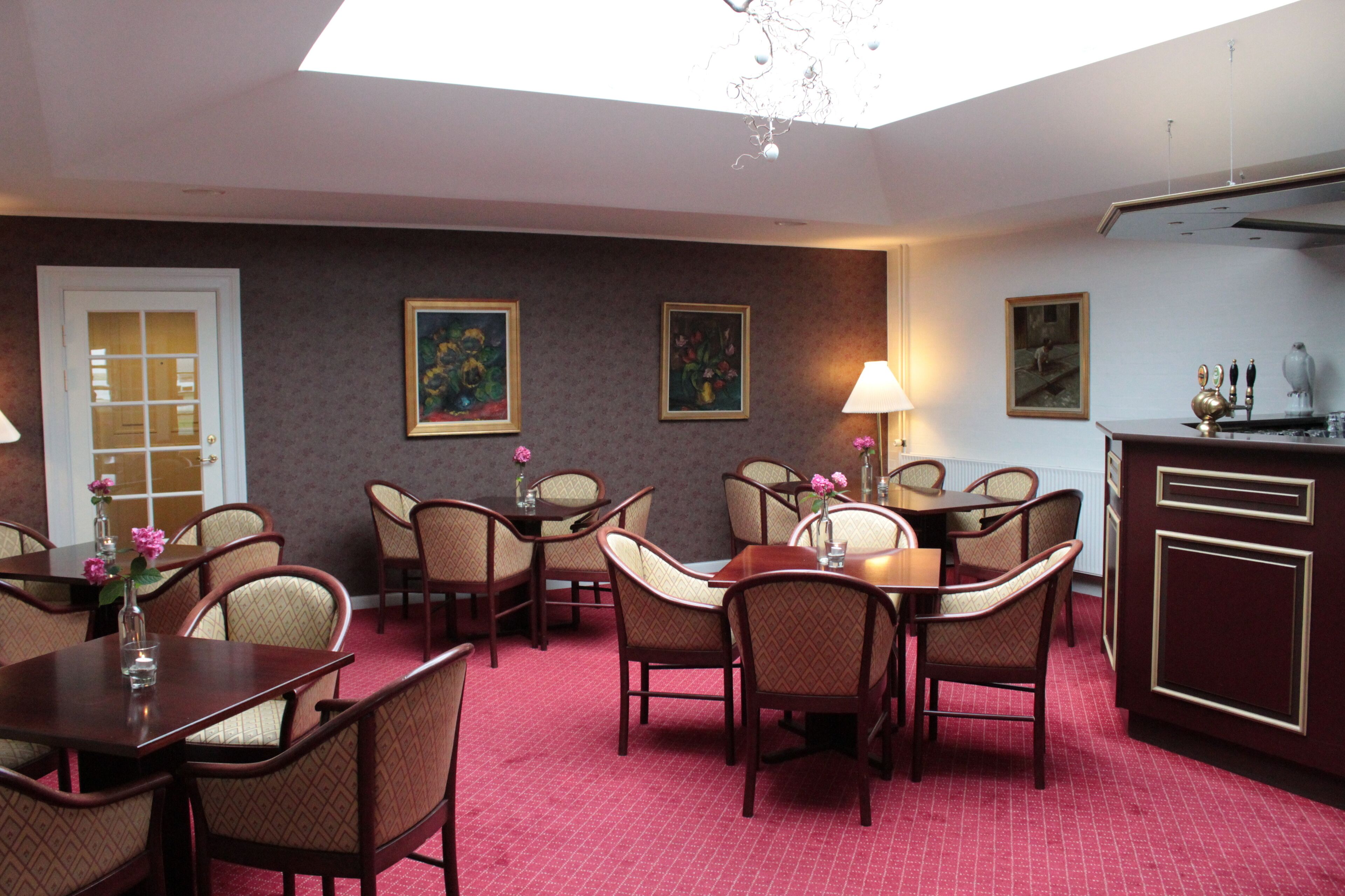 A dining area with multiple tables and chairs, a chandelier, and framed artwork on the walls.