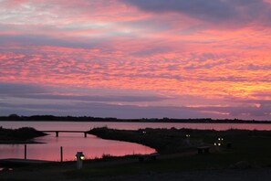 Un coucher de soleil sur un lac paisible, avec un pont et une rive éloignée.