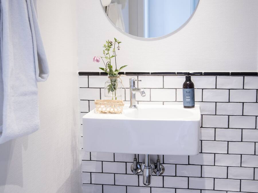A bathroom with a white sink, a round mirror, and a black and white tiled backsplash.