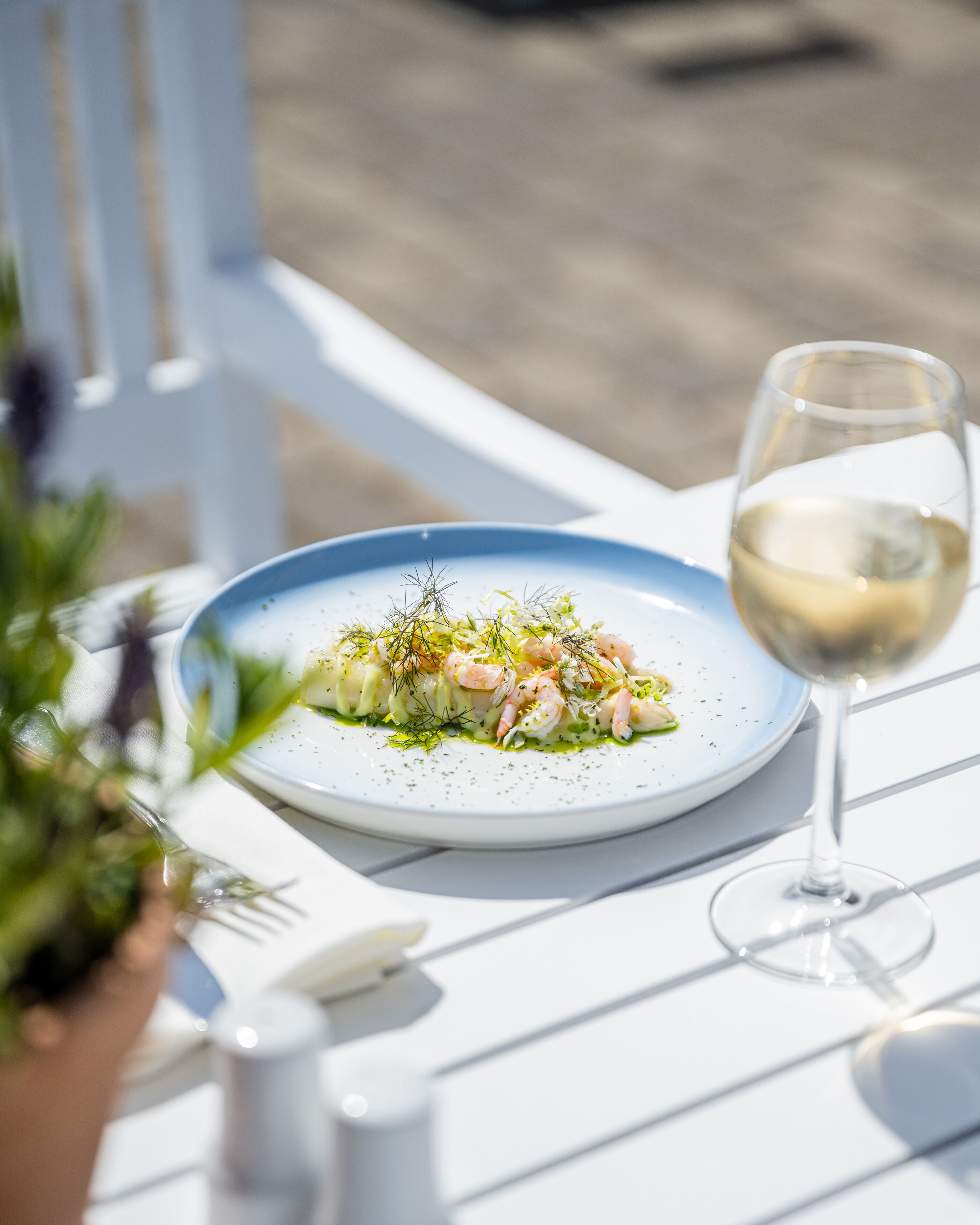 A white table with a plate of food and a glass of white wine.