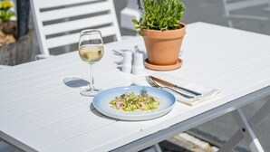 Ein Tisch mit einem Teller Essen, einem Glas Weißwein und einer Topfpflanze.