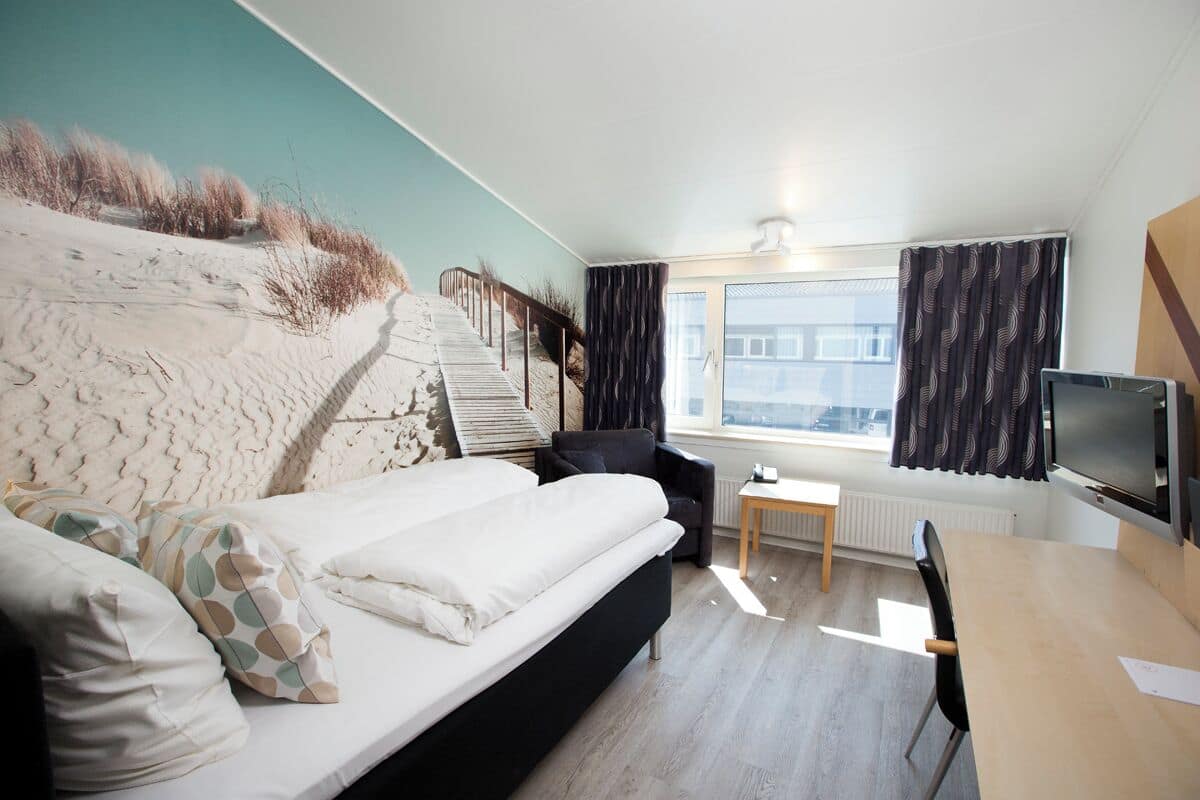 A modern bedroom with a bed, a desk, a chair, and a TV.