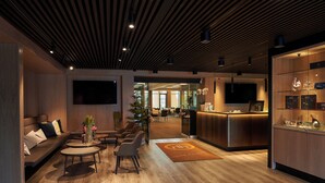 A modern lobby with a reception desk, seating area, and a large TV screen. - Hotel Hedegaarden (Vejle)