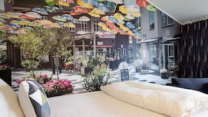 A hotel room with a bed, pillows, and a view of the street with umbrellas and shops. - Hotel Hedegaarden (Vejle)