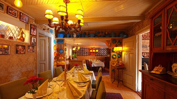 A dining area with a long table set for a meal, a chandelier, and a wall decorated with plates. - Låsby Kro og Hotel (Lasby)