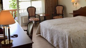 A hotel room with a large bed, a desk with a lamp, two chairs, a small table, and a window with curtains. - Låsby Kro og Hotel (Lasby)