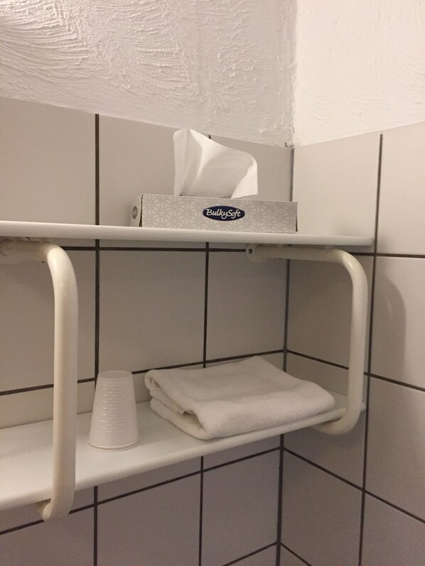 Un baño con un estante blanco que sostiene una caja de pañuelos y una toalla doblada.