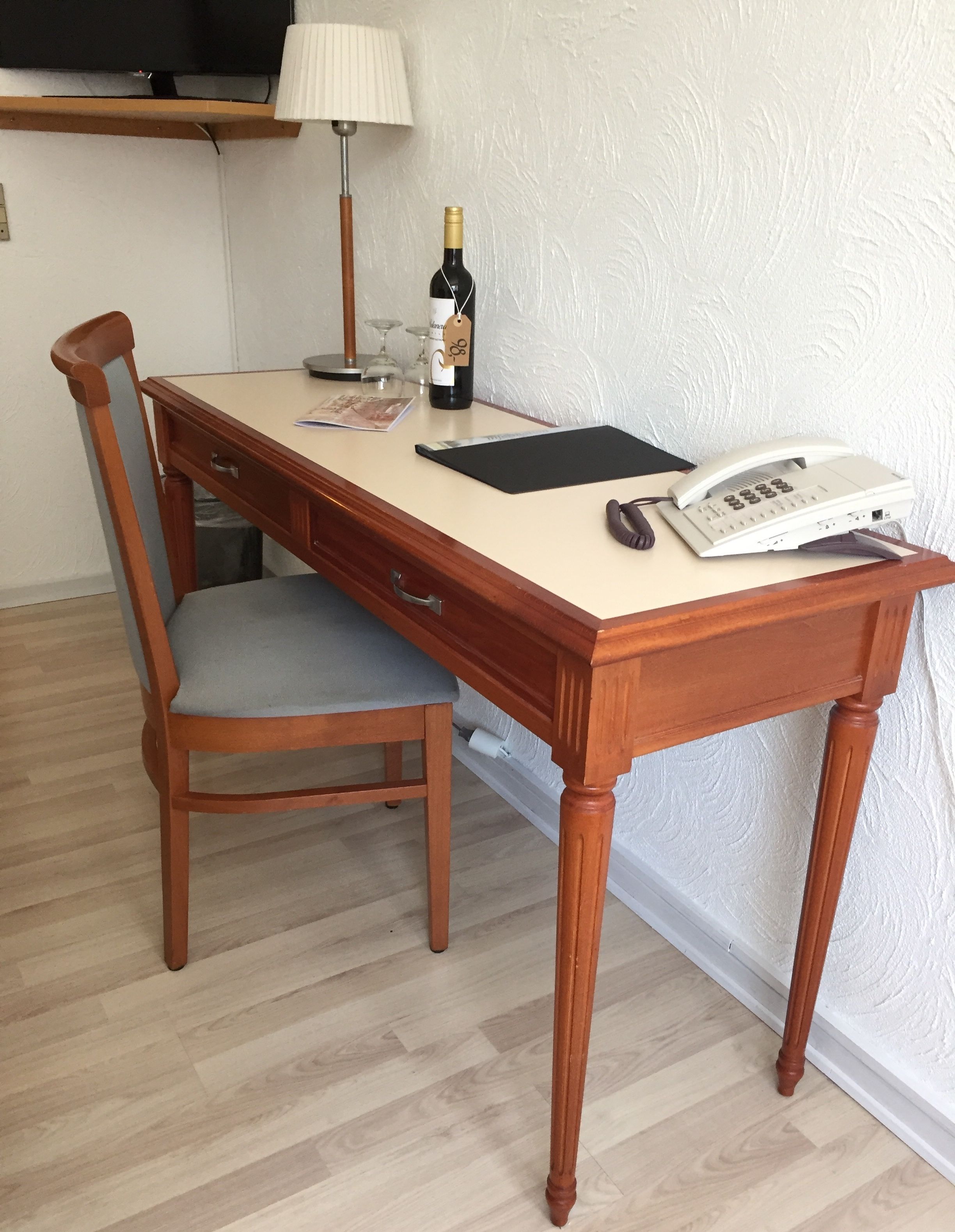 A wooden desk with a chair, a bottle of wine, a lamp, and a telephone.