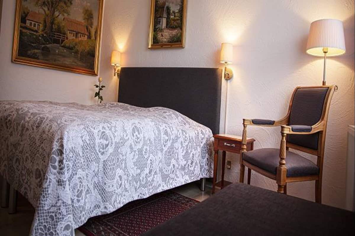Une chambre d’hôtel avec un lit, une chaise et deux lampes fixées au mur.
