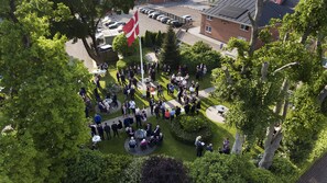 Ein Außenbereich für Zusammenkünfte mit Fahnenmast, umgeben von Bäumen und einem Parkplatz.
