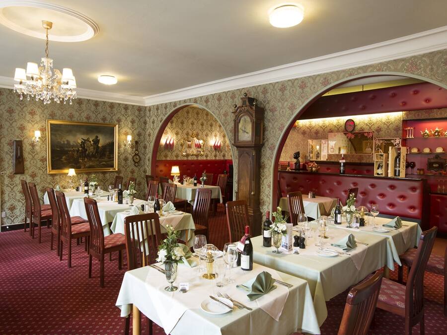 Uma sala de jantar formal, com mesas postas, um candelabro e um relógio na parede.