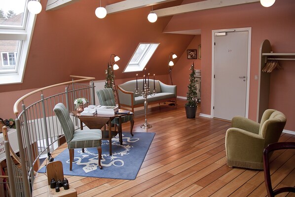 A cozy loft-style room with a wooden floor, a blue rug, a dining table with chairs, a sofa, and a small Christmas tree.