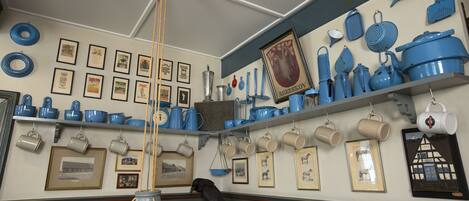 A kitchen with blue and white cookware, framed pictures on the walls, and a hanging light fixture.
