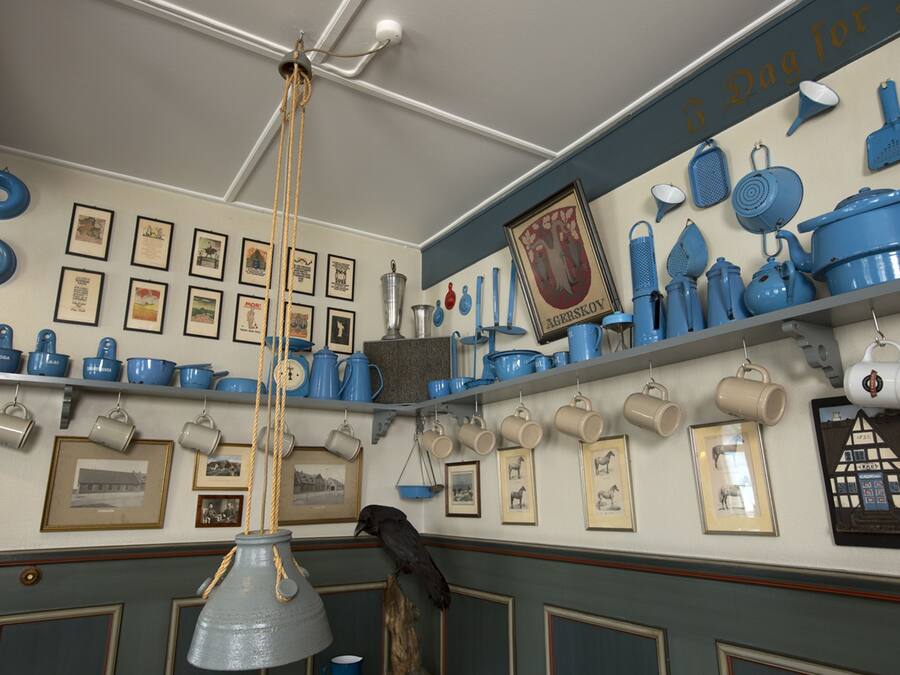 Una cocina con utensilios de cocina azules y blancos, cuadros en las paredes y una lámpara colgante.