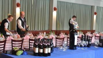 A formal dining setup with multiple tables, each set with wine bottles, glasses, and waitstaff serving.