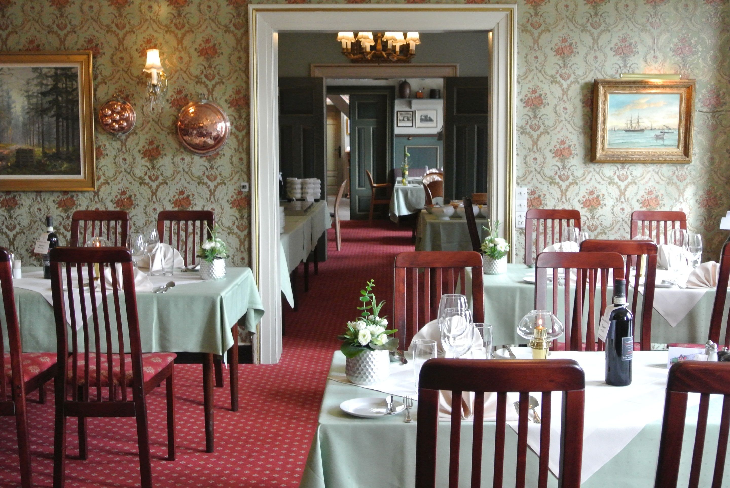 A dining area with tables set for service, wooden chairs, and a red carpet.