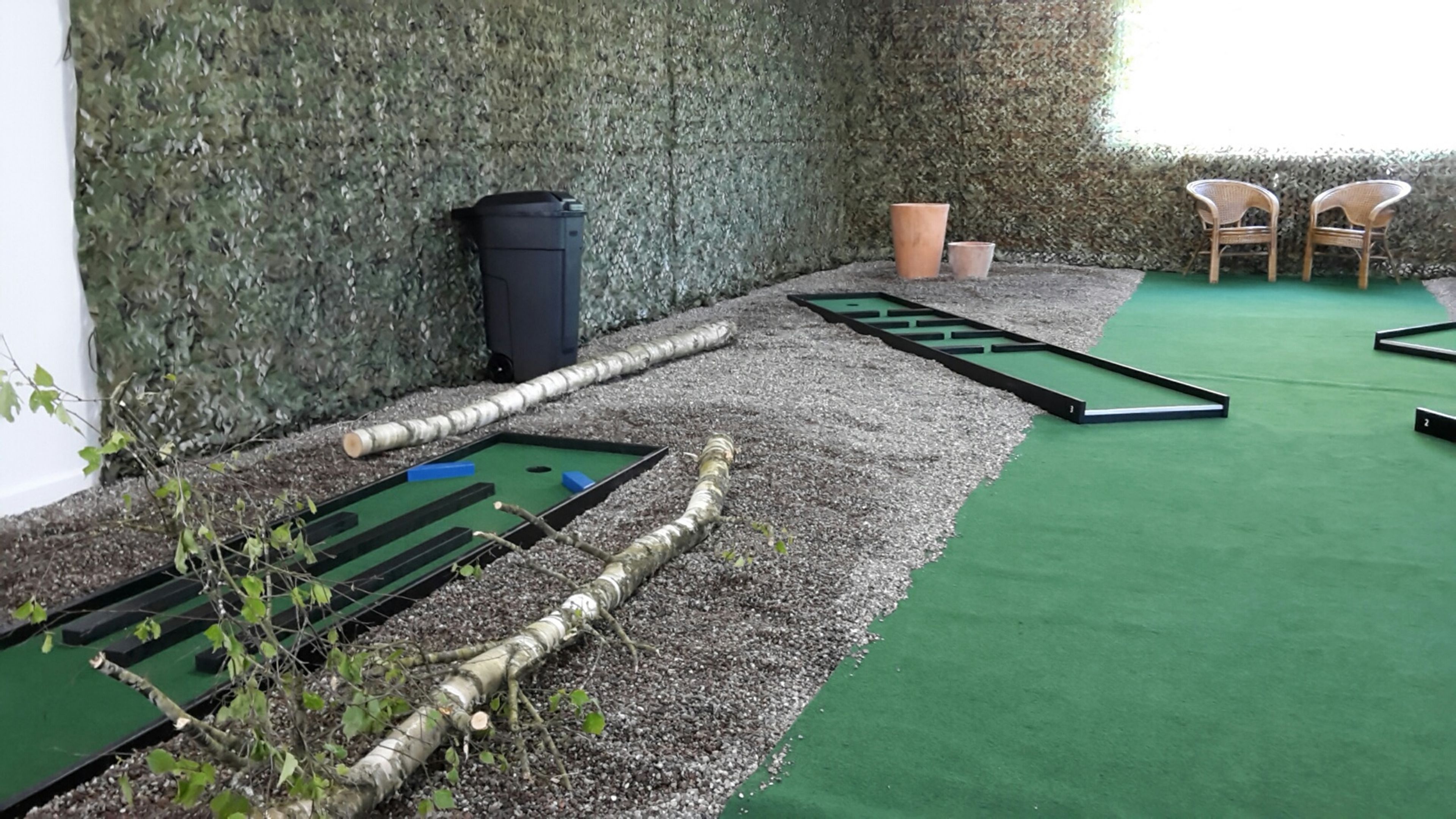 A billiards setup with multiple tables, a trash bin, and two wicker chairs.
