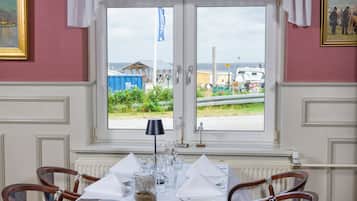 Comedor con una mesa dispuesta para cuatro personas, dos sillas a cada lado, una ventana con vistas al exterior y una cortina blanca sobre la ventana.