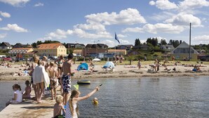 A wooden pier extending into a calm body of water with people sitting and standing on it.