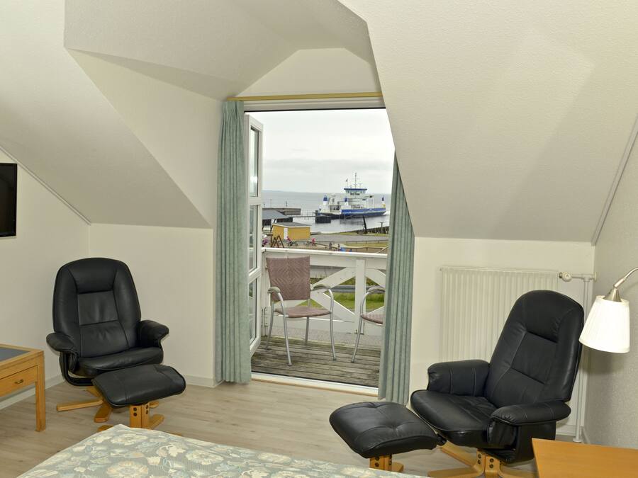 A room with a balcony, two black leather chairs, a wooden table, a small sofa, and a lamp.