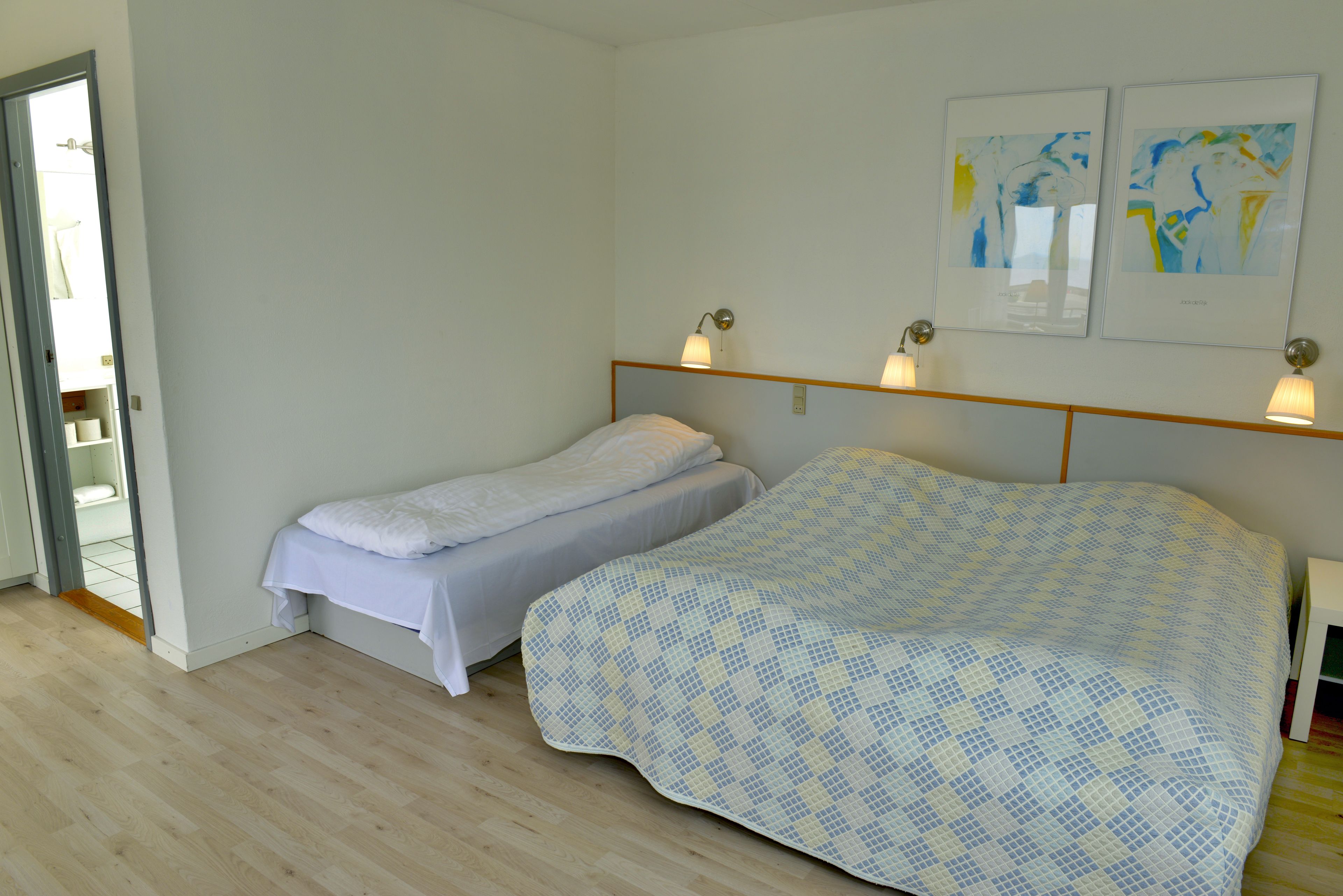 Ein Schlafzimmer mit zwei Betten, Holzboden, einer Tür zu einem Badezimmer und zwei Wandlampen.