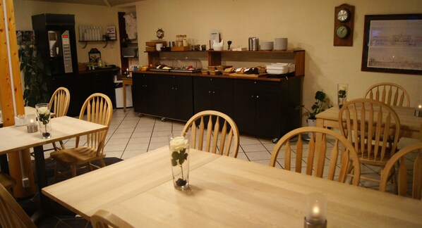 A dining area with wooden tables and chairs, a buffet counter with food and drinks, and a coffee machine. - Hvalpsund Færgekro (Farso)