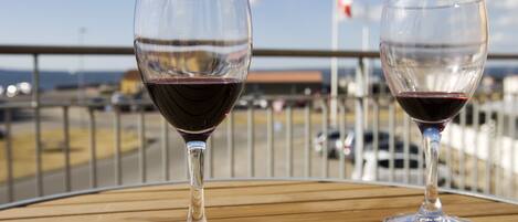 Dos copas de vino sobre una mesa de madera, con una vista de una bandera y una carretera al fondo.