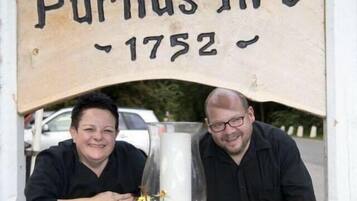 Ein hölzernes Schild mit der Aufschrift 'Purhus Kro 1752' über einem Blumenbeet.