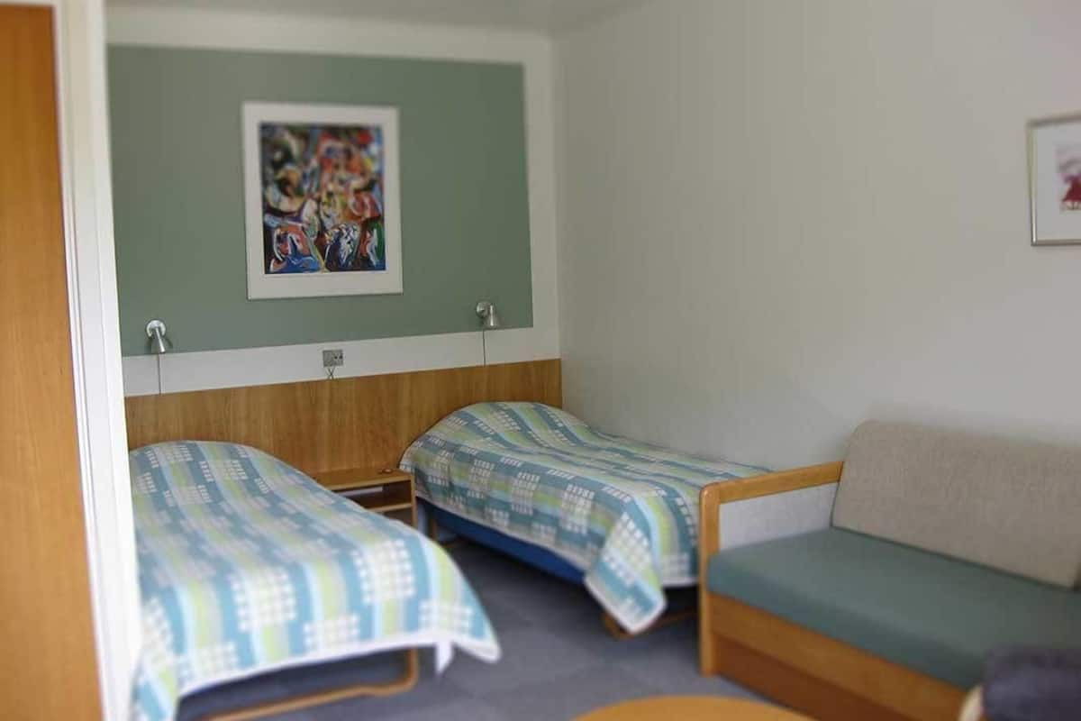 Une chambre avec deux lits simples et un canapé, un tableau au mur et une petite table ronde.