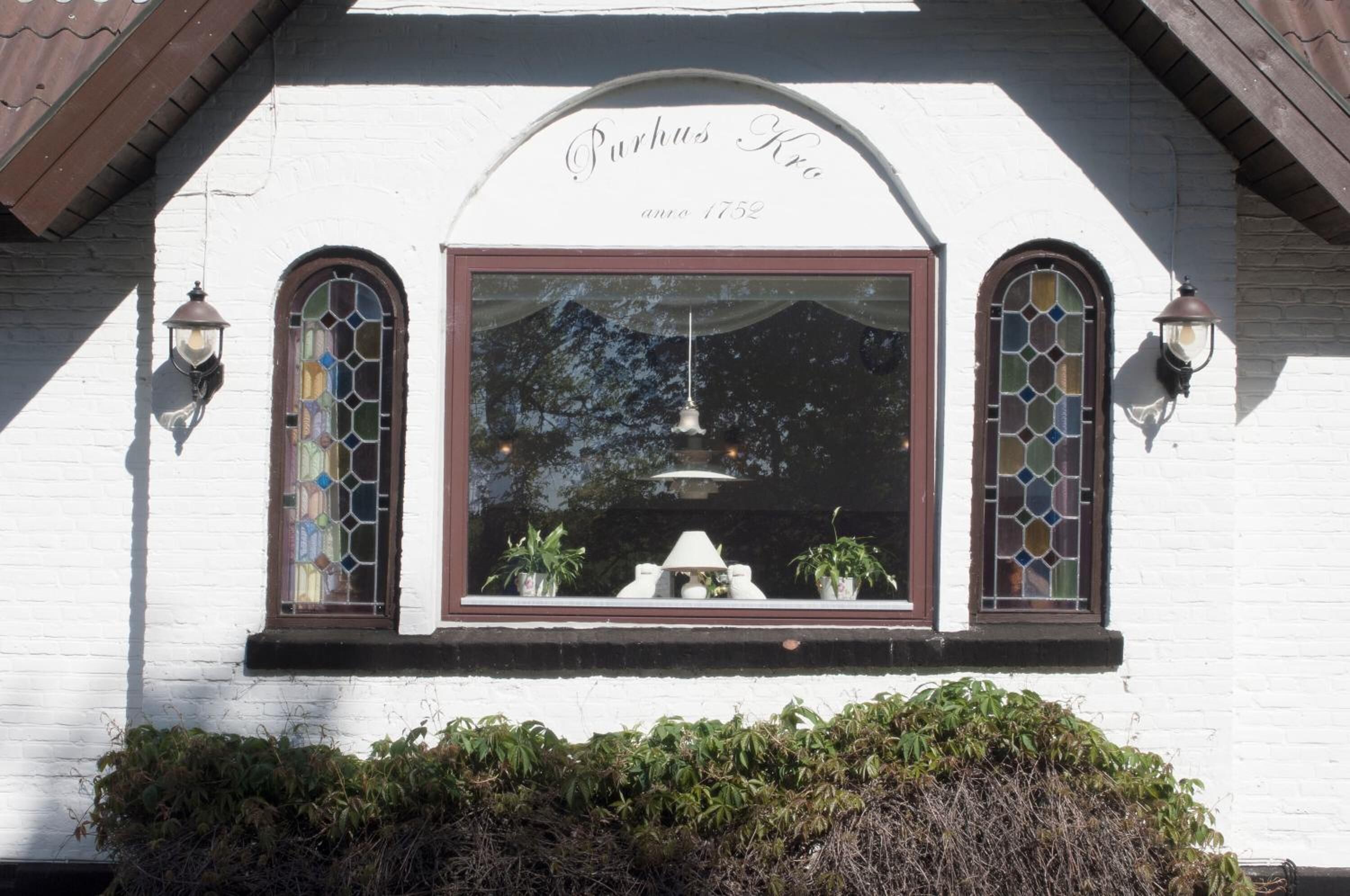 Un edificio con fachada blanca, dos ventanas arqueadas con vidrieras, y un letrero sobre las ventanas que dice 
