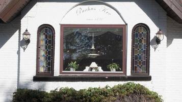 Un edificio con fachada blanca, dos ventanas arqueadas con vidrieras, y un letrero sobre las ventanas que dice
