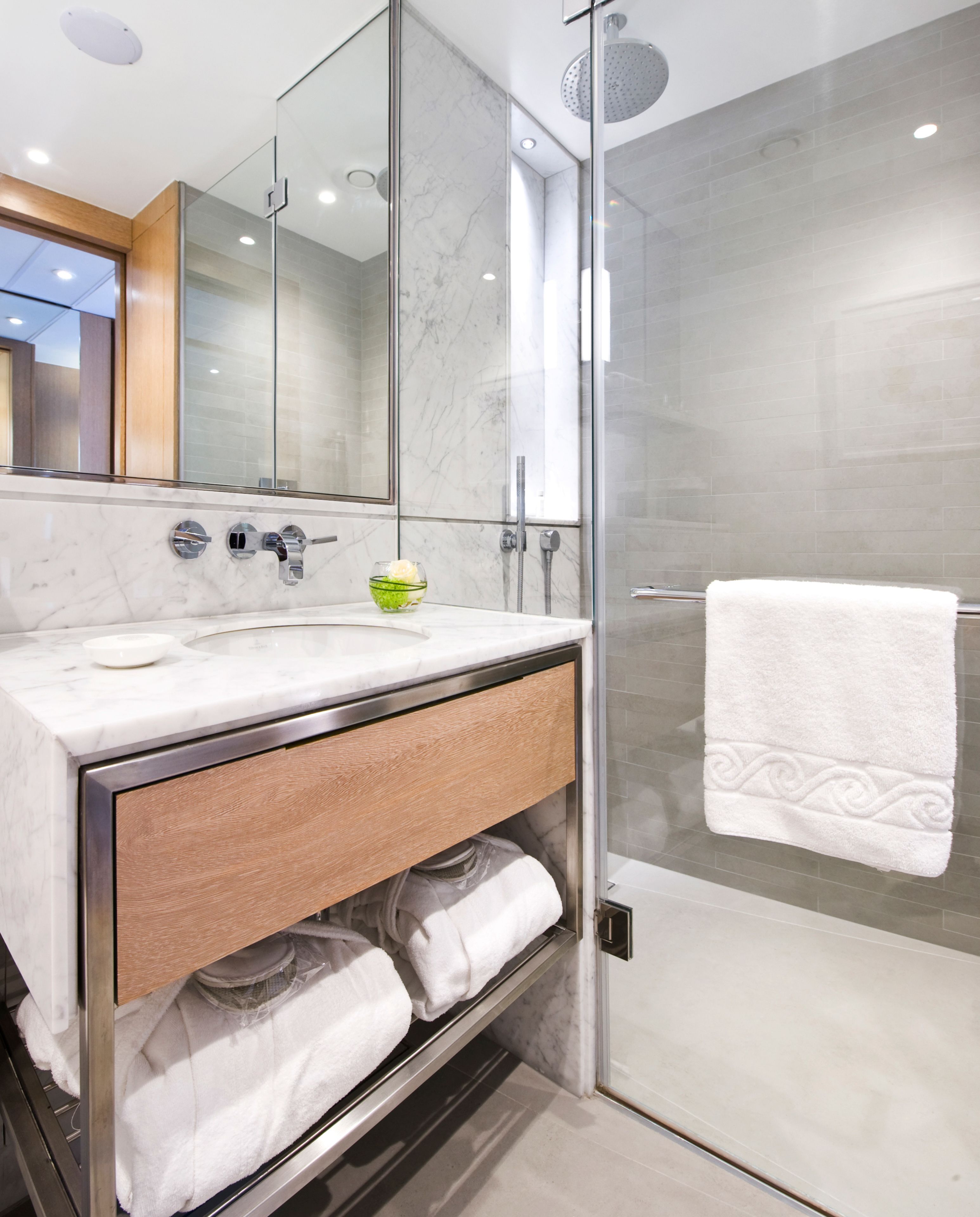A modern bathroom with a glass shower enclosure, a marble countertop, and a towel rack.