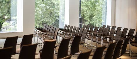 Un salón de conferencias con filas de sillas frente a un ventanal con vistas a árboles.