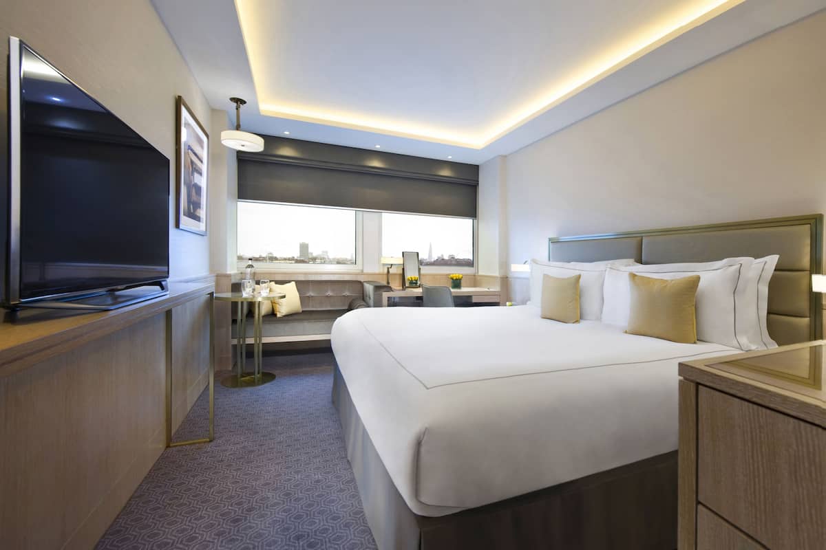 A modern hotel room with a large bed, a desk, a TV, and a city view.