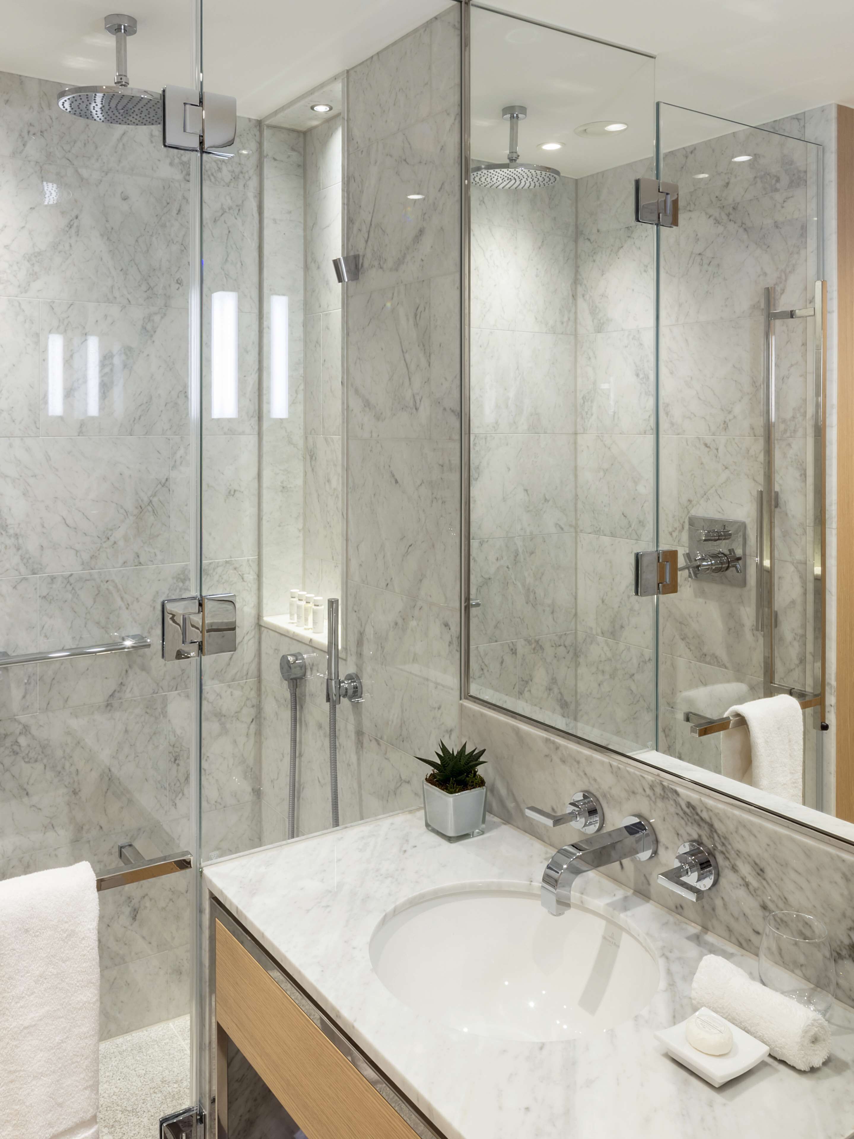 A modern bathroom with a glass shower enclosure, a marble sink, and a large mirror.