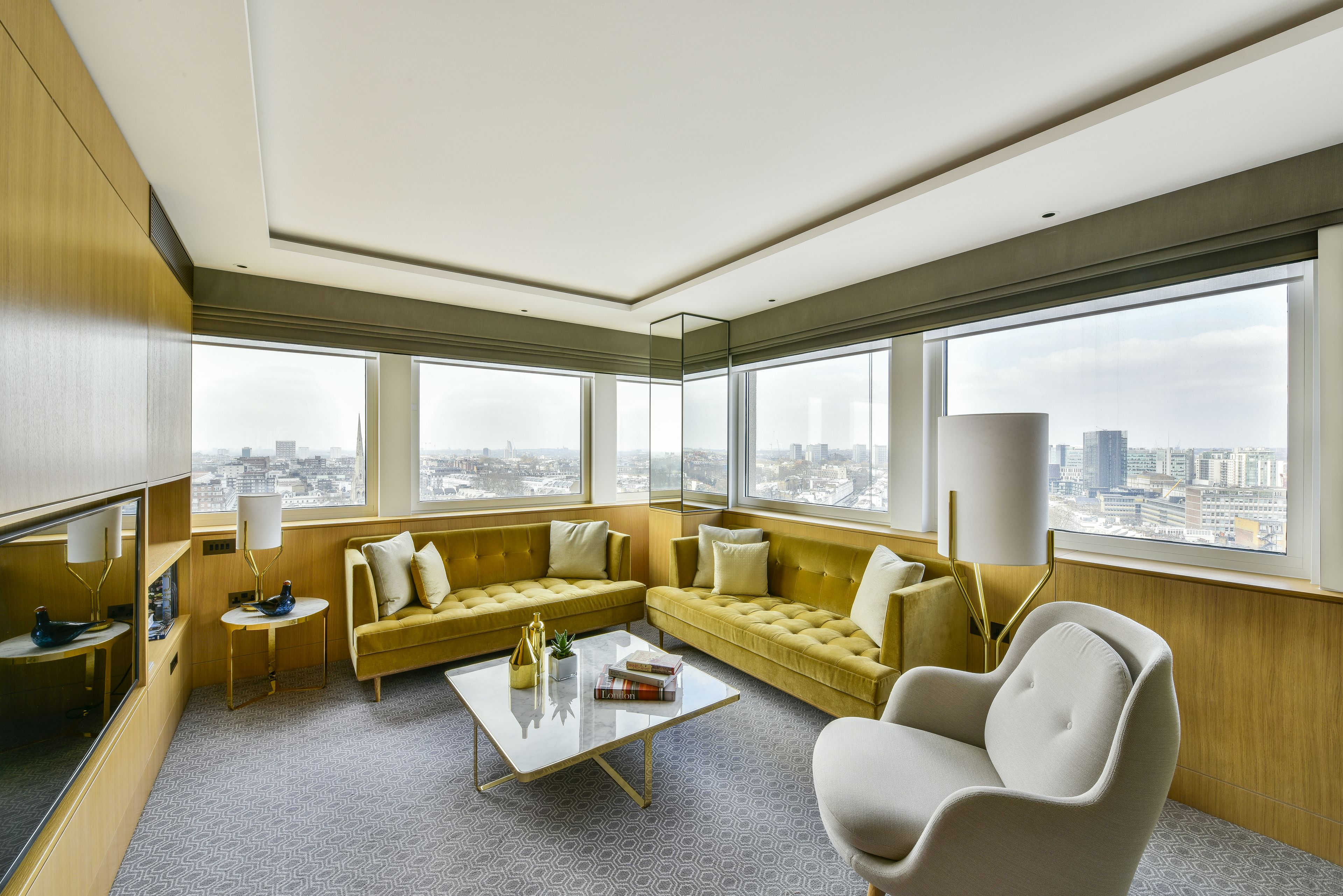 A modern hotel room with a large window, a sofa, a coffee table, and a chair.