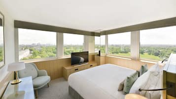 Habitación de hotel moderna con una cama grande, televisión, sillón y vistas a la ciudad y zonas verdes.