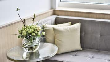 A round glass table with a vase of flowers in a clear glass bowl, placed on a grey sofa with a cushion.