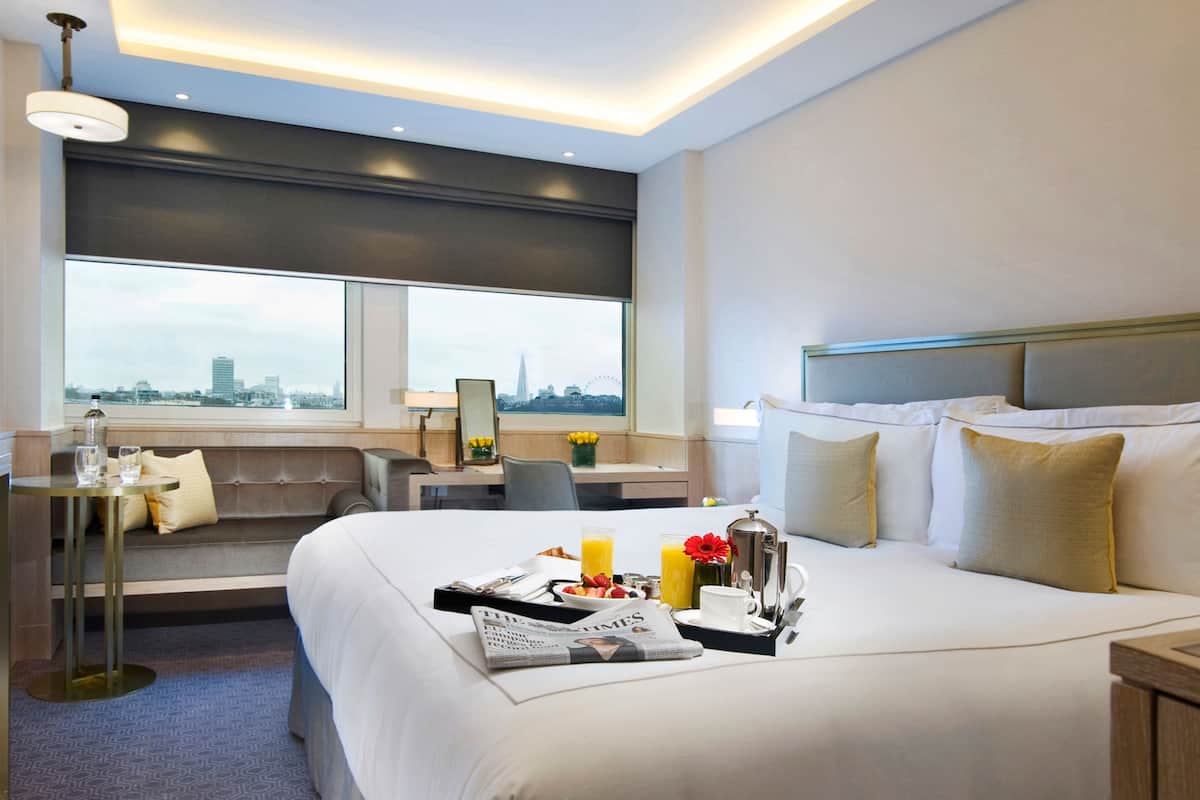A hotel room with a large bed, a seating area with a view, and a breakfast tray on the bed.