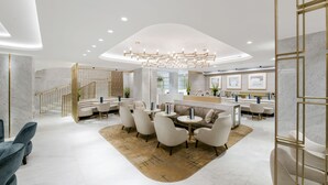A modern hotel lobby with a central seating area, a staircase, and a reception desk. - Royal Lancaster London (London)