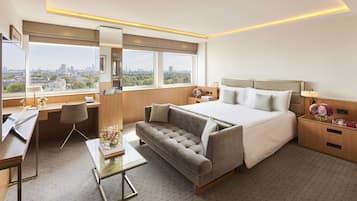 A modern hotel room with a large bed, a sofa, a desk, and a view of the city.
