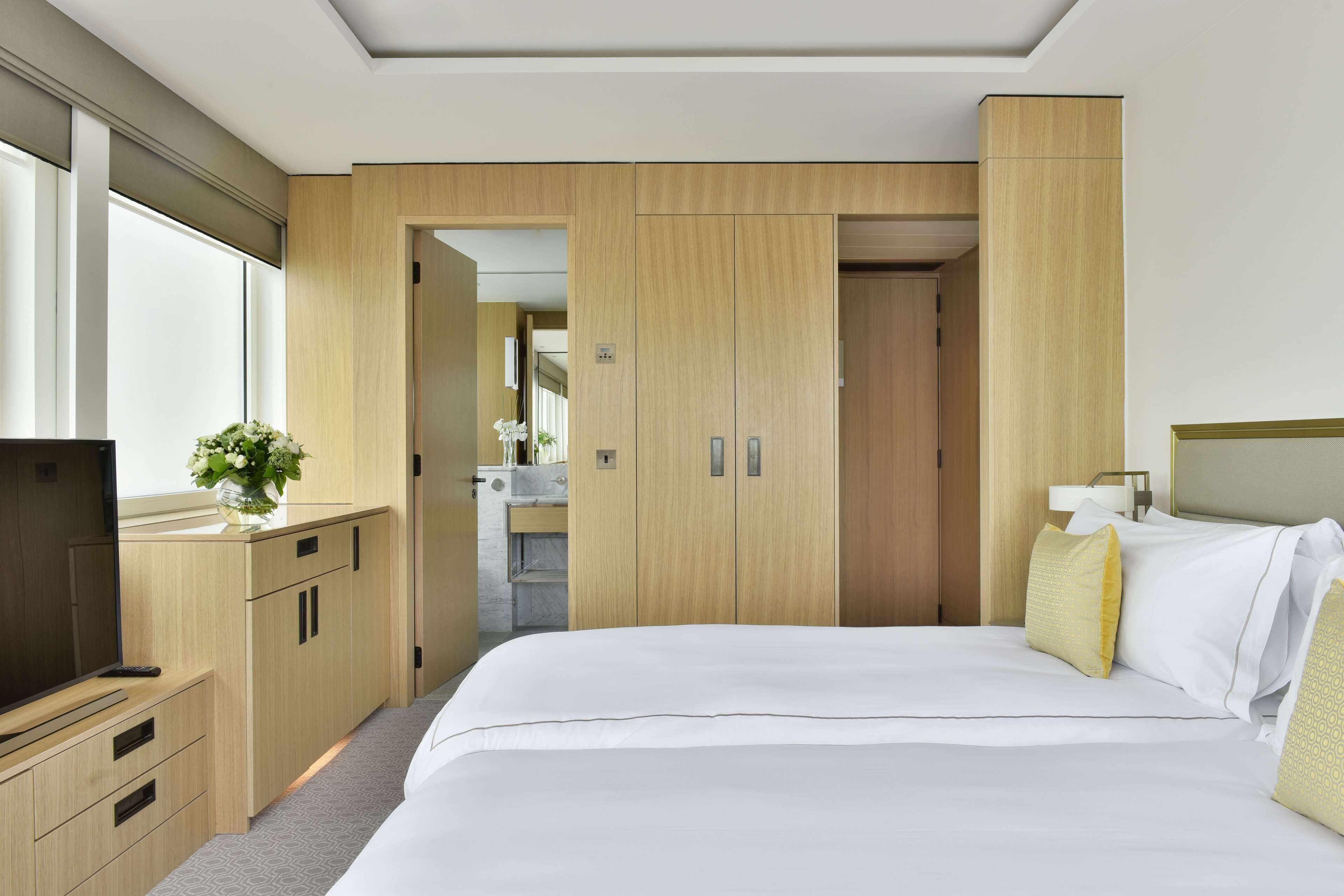 A hotel room with a large bed, wooden wardrobe, a television, and a small table with a vase of flowers.