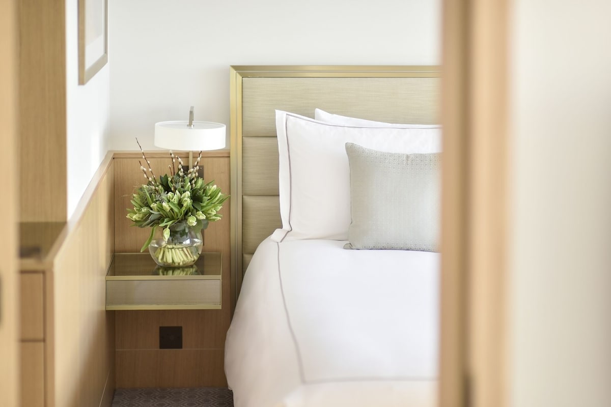 Ein Hotelzimmer mit einem Bett, einem Nachttisch mit Lampe und Blumenvase sowie einem Holzkopfteil.