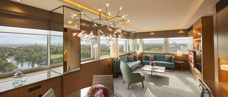 A modern hotel room with a large window offering a city view, a stylish chandelier, and a cozy seating area.