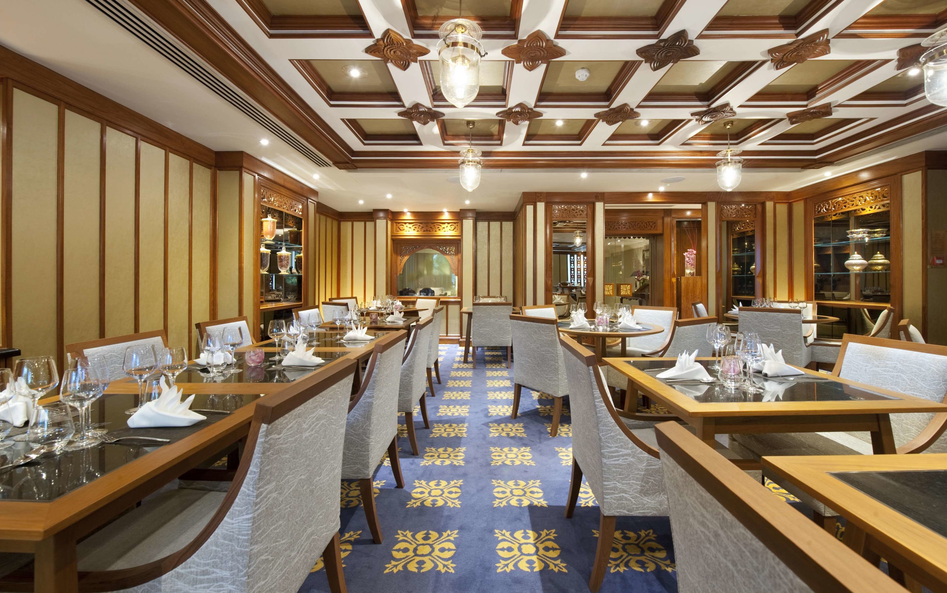 A restaurant with wooden tables and chairs, a patterned carpet, and a decorative ceiling.